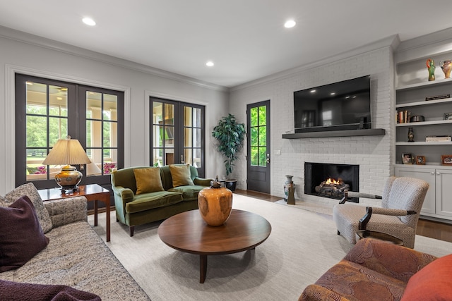 living room with light hardwood / wood-style floors, ornamental molding, a brick fireplace, built in features, and french doors