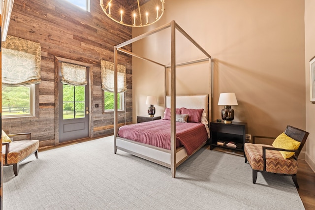 bedroom featuring access to outside, wood walls, a chandelier, and a high ceiling