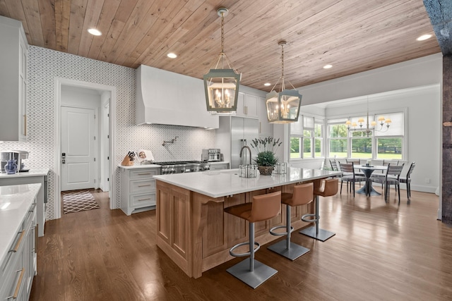 kitchen with dark wood-type flooring, a center island with sink, decorative light fixtures, and white cabinets