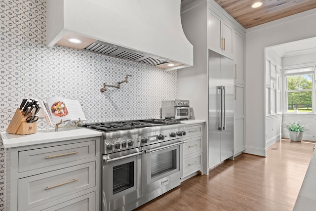 kitchen with ornamental molding, backsplash, dark wood-type flooring, high quality appliances, and premium range hood