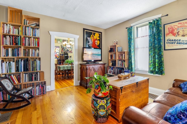 living area featuring wood finished floors, baseboards, visible vents, a textured ceiling, and a notable chandelier
