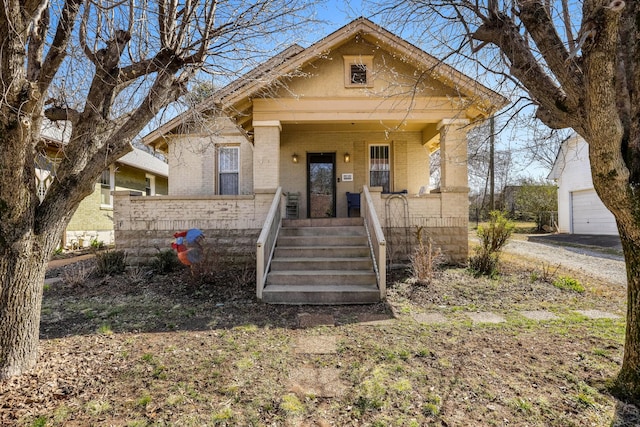 bungalow-style home with brick siding, covered porch, and an outdoor structure