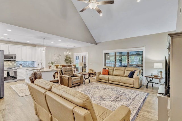 living room featuring light hardwood / wood-style floors, ceiling fan with notable chandelier, sink, and high vaulted ceiling