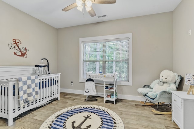 bedroom featuring light wood-type flooring, ceiling fan, and a crib