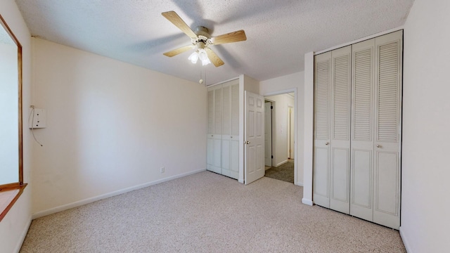 unfurnished bedroom featuring ceiling fan, a textured ceiling, light carpet, and multiple closets