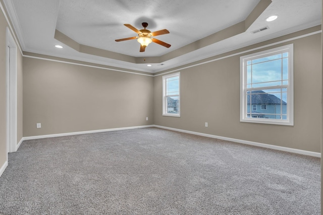 empty room featuring a raised ceiling, crown molding, carpet, and ceiling fan