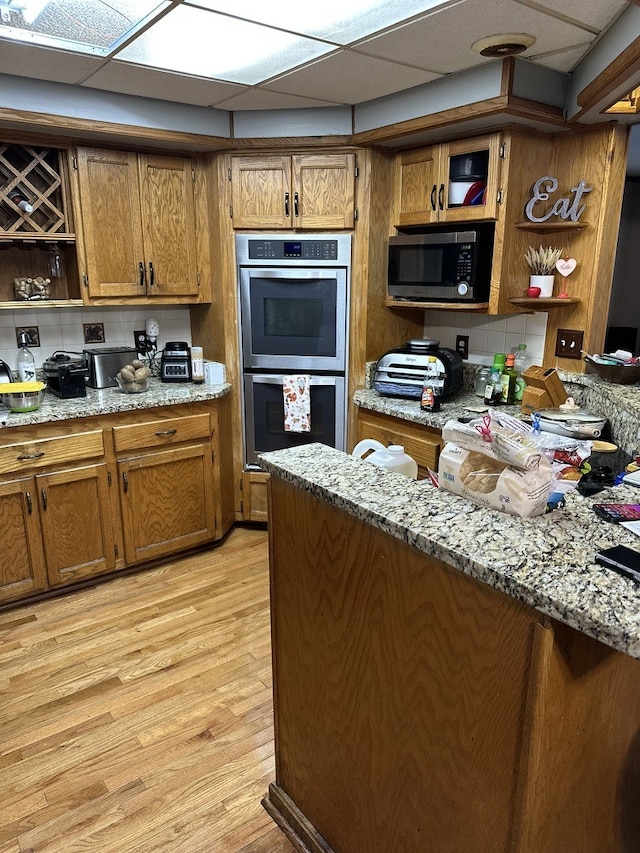 kitchen featuring stainless steel appliances, light wood-type flooring, backsplash, light stone countertops, and a drop ceiling