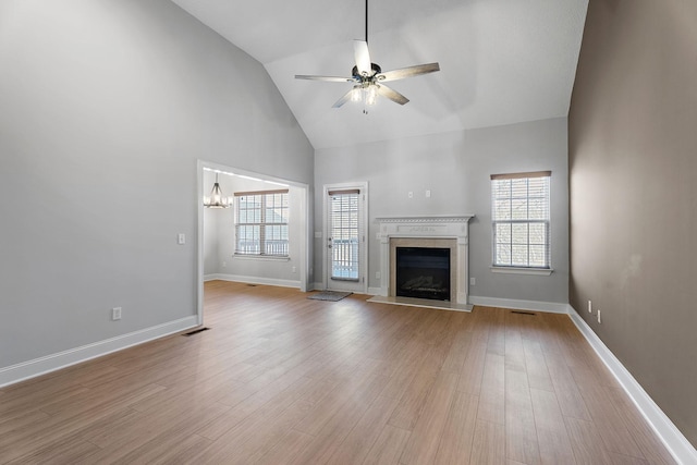 unfurnished living room featuring high vaulted ceiling, ceiling fan with notable chandelier, and light wood-type flooring