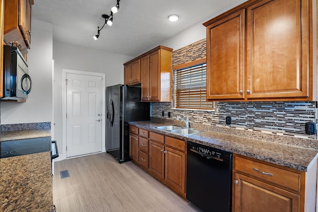 kitchen featuring sink, dark stone counters, decorative backsplash, black appliances, and light wood-type flooring