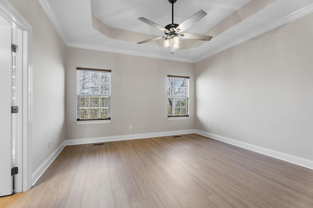 empty room featuring crown molding, ceiling fan, a raised ceiling, and light wood-type flooring