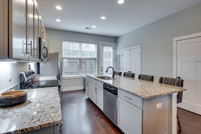 kitchen featuring a center island with sink, appliances with stainless steel finishes, sink, a kitchen breakfast bar, and dark wood-type flooring