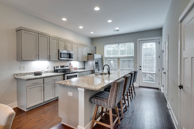 kitchen with stainless steel appliances, gray cabinets, sink, dark wood-type flooring, and a kitchen island with sink