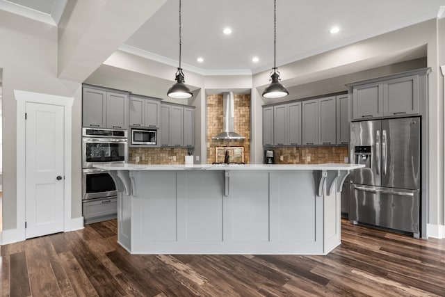 kitchen featuring stainless steel appliances, wall chimney range hood, a kitchen breakfast bar, and gray cabinetry