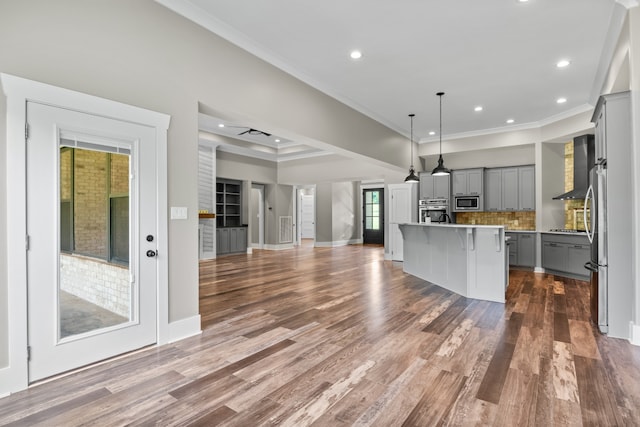 kitchen with stainless steel appliances, an island with sink, wood-type flooring, gray cabinetry, and pendant lighting