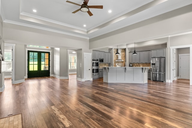 unfurnished living room featuring french doors, dark wood-type flooring, ornamental molding, ceiling fan, and a tray ceiling