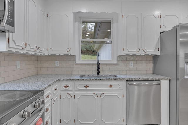 kitchen featuring light stone counters, backsplash, appliances with stainless steel finishes, sink, and white cabinets