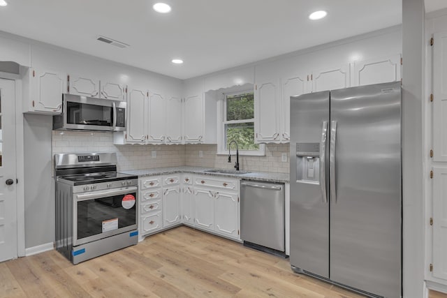 kitchen featuring light hardwood / wood-style floors, stainless steel appliances, white cabinets, decorative backsplash, and sink