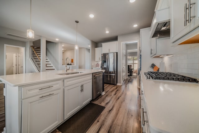 kitchen featuring a center island with sink, sink, hanging light fixtures, white cabinetry, and stainless steel appliances