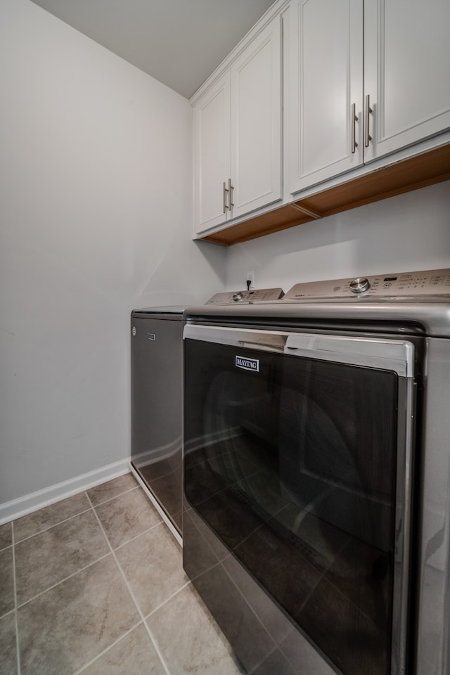 laundry area featuring washing machine and dryer, light tile patterned floors, and cabinets