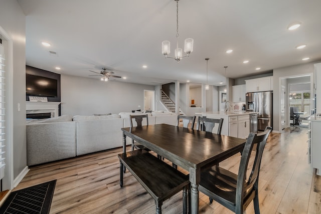 dining space featuring ceiling fan with notable chandelier, sink, and light hardwood / wood-style flooring