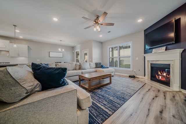 living room with light hardwood / wood-style floors, ceiling fan, and a premium fireplace