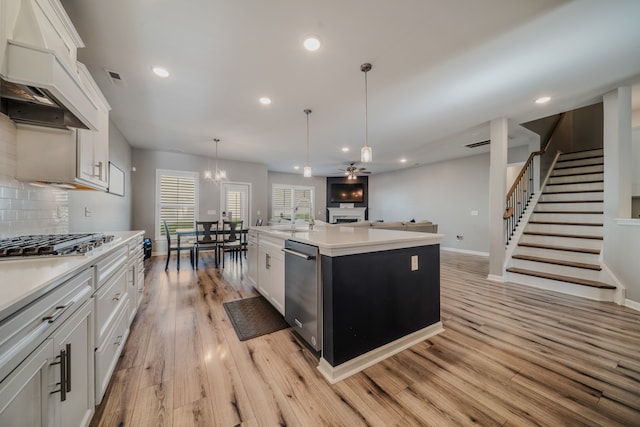 kitchen with a kitchen island with sink, white cabinets, stainless steel appliances, and decorative light fixtures