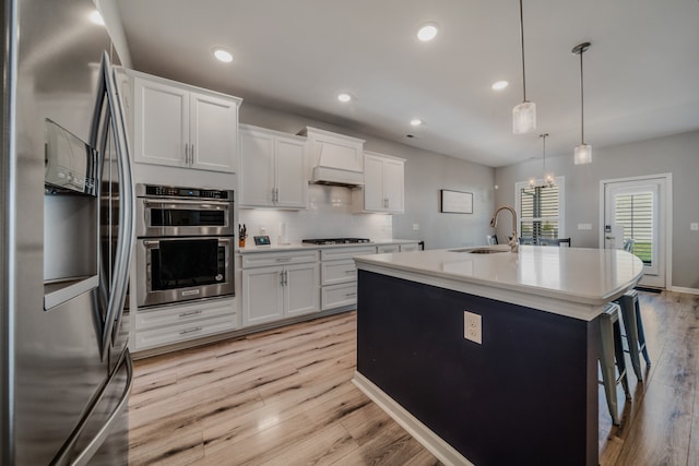 kitchen with white cabinetry, sink, hanging light fixtures, an island with sink, and appliances with stainless steel finishes