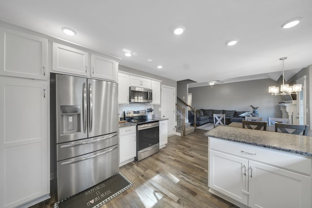 kitchen with appliances with stainless steel finishes, hardwood / wood-style floors, stone counters, white cabinets, and decorative backsplash