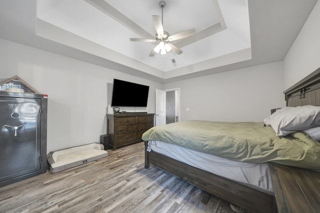 bedroom with hardwood / wood-style flooring, ceiling fan, and a raised ceiling