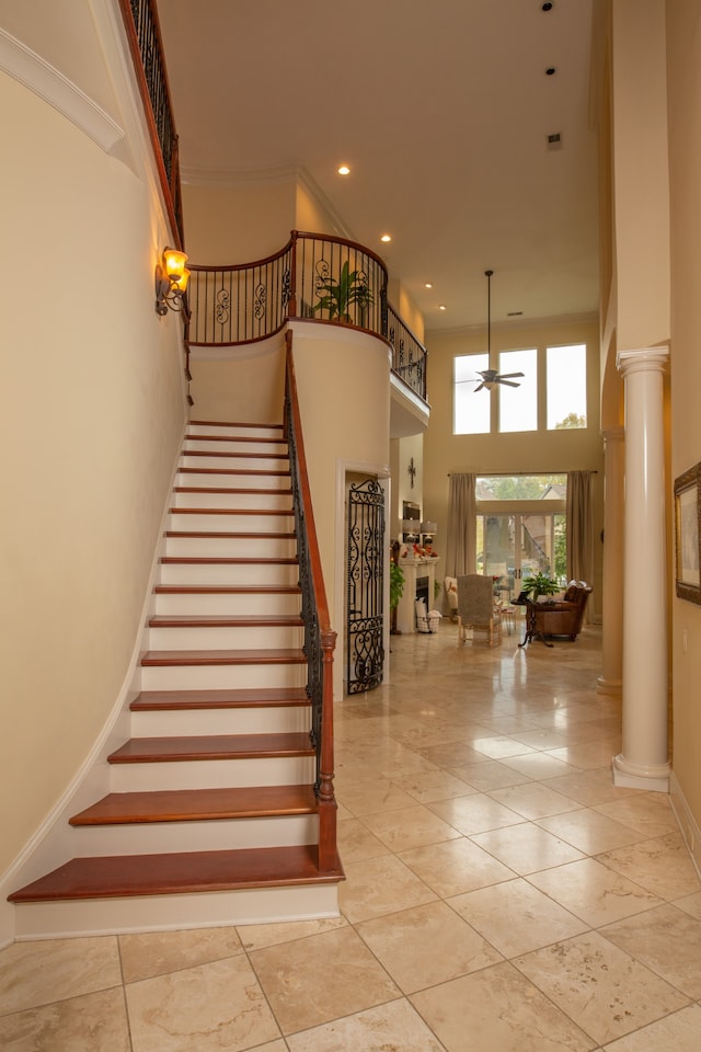 stairs with a high ceiling, ceiling fan, and ornate columns