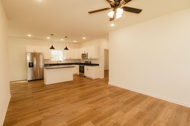 kitchen featuring light wood-type flooring, appliances with stainless steel finishes, a center island, and decorative light fixtures