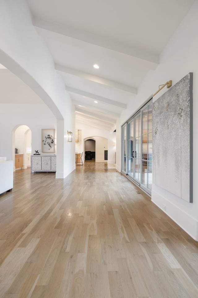 unfurnished living room featuring light wood-type flooring and lofted ceiling with beams