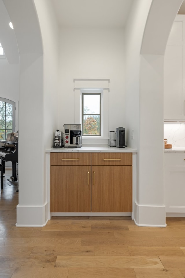 bar featuring white cabinets, light wood-type flooring, a wealth of natural light, and backsplash