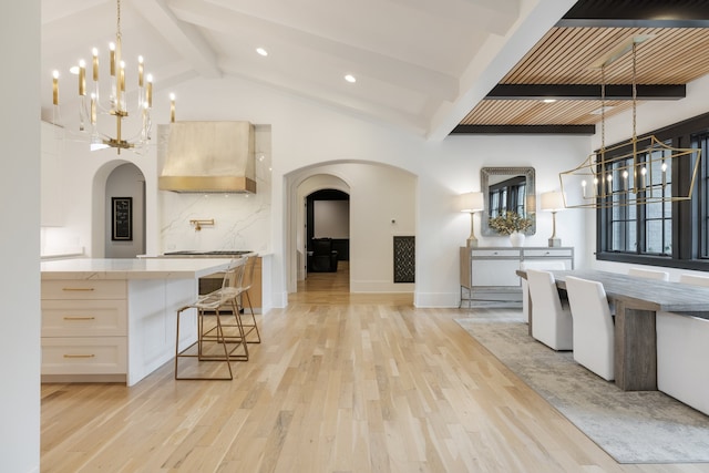 kitchen with light hardwood / wood-style floors, light brown cabinetry, wall chimney range hood, and vaulted ceiling with beams