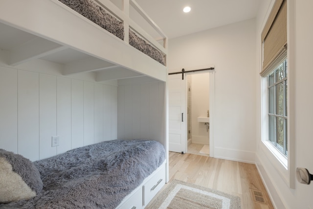 bedroom featuring a barn door, ensuite bathroom, multiple windows, and light wood-type flooring