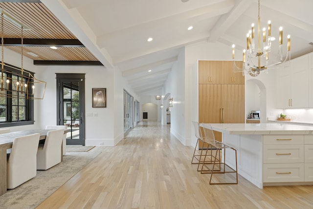 kitchen with a kitchen breakfast bar, hanging light fixtures, vaulted ceiling with beams, light hardwood / wood-style flooring, and white cabinets