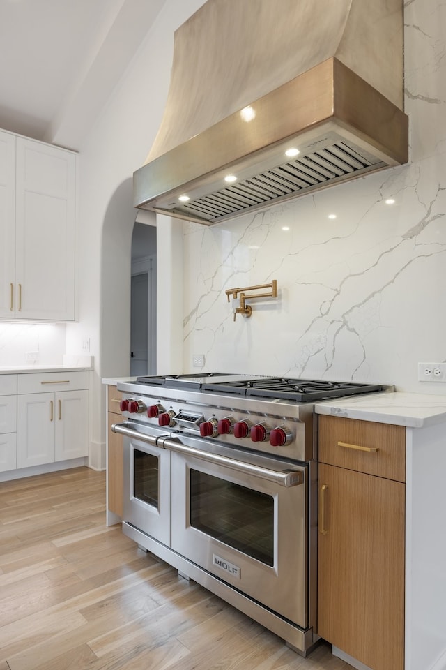 kitchen with light hardwood / wood-style floors, tasteful backsplash, white cabinetry, premium range hood, and luxury range