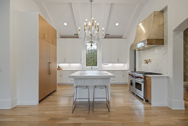 kitchen with double oven range, a kitchen island, white cabinets, wall chimney range hood, and lofted ceiling with beams