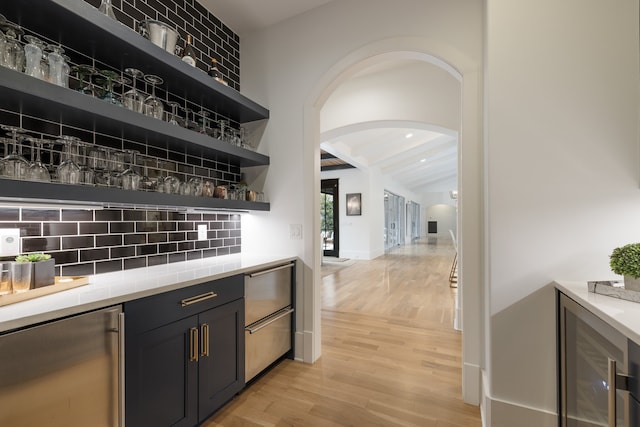 bar with backsplash, beam ceiling, stainless steel fridge, and light hardwood / wood-style flooring