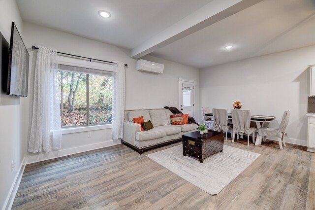 living room featuring light hardwood / wood-style flooring, an AC wall unit, and beam ceiling