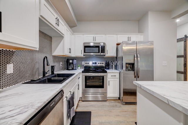 kitchen featuring white cabinetry, sink, appliances with stainless steel finishes, light hardwood / wood-style flooring, and a barn door