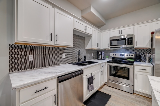 kitchen with light hardwood / wood-style floors, white cabinetry, sink, appliances with stainless steel finishes, and decorative backsplash