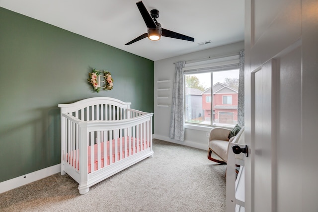 carpeted bedroom featuring a crib and ceiling fan