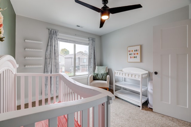 carpeted bedroom featuring a crib and ceiling fan