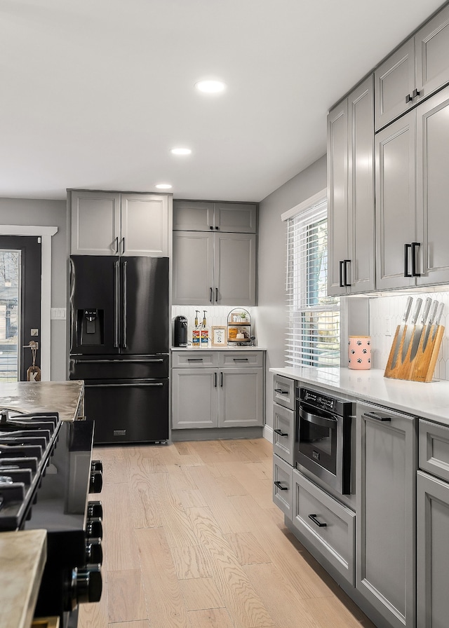 kitchen featuring stainless steel oven, light wood-type flooring, range, gray cabinets, and high end black fridge