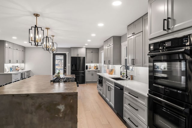 kitchen with black appliances, sink, gray cabinets, a kitchen island, and light wood-type flooring