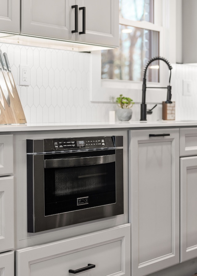 details with stainless steel oven, white cabinetry, and backsplash