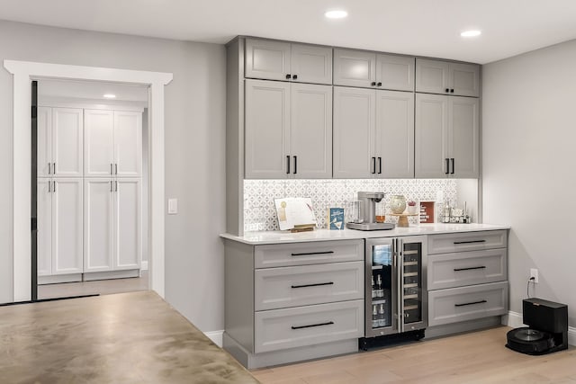 bar with decorative backsplash, light hardwood / wood-style floors, gray cabinets, and wine cooler