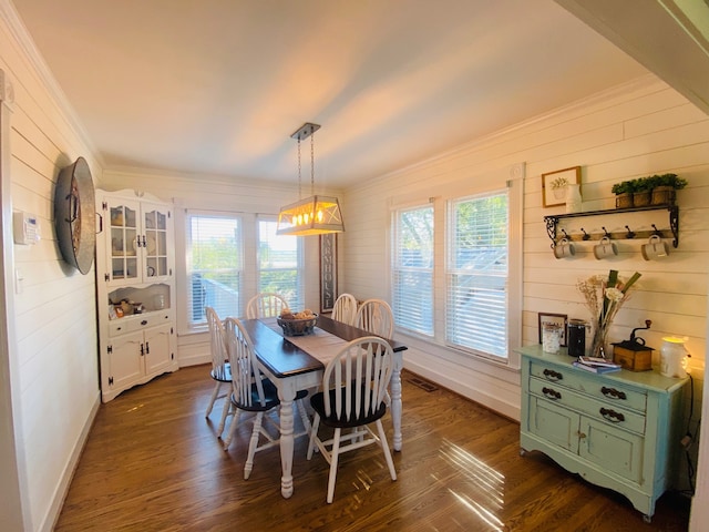 dining space featuring dark wood-type flooring, wood walls, crown molding, and plenty of natural light