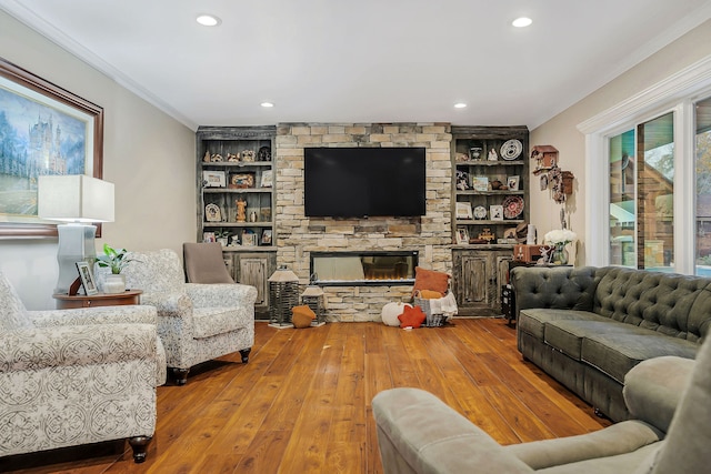 living room featuring built in shelves, a fireplace, crown molding, and light hardwood / wood-style flooring